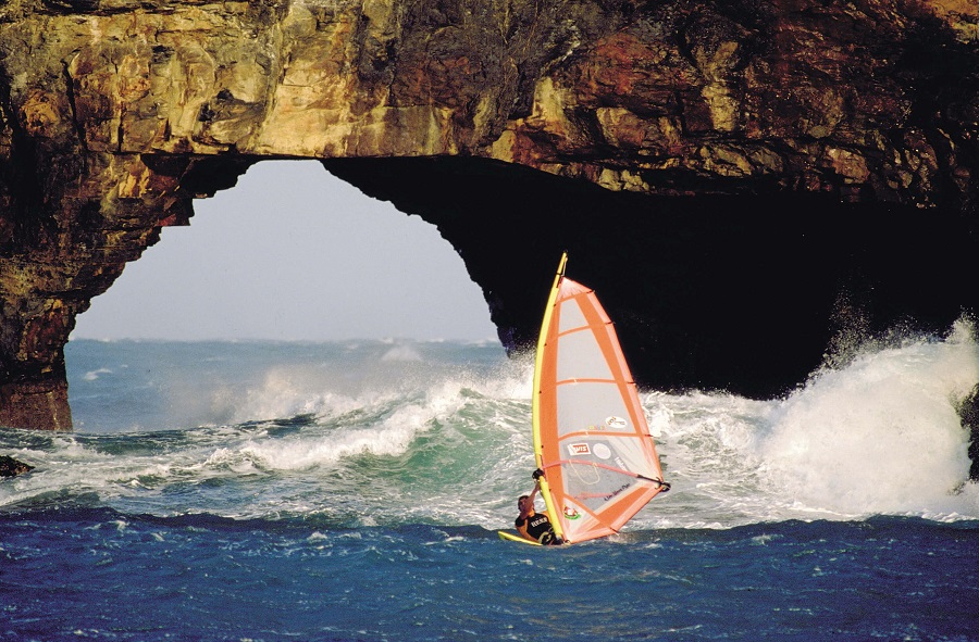 A windsurfer passing the rock arch at Hole in the Wall