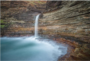 Waterfall Bluff cascading over layered coastal cliffs into the sea